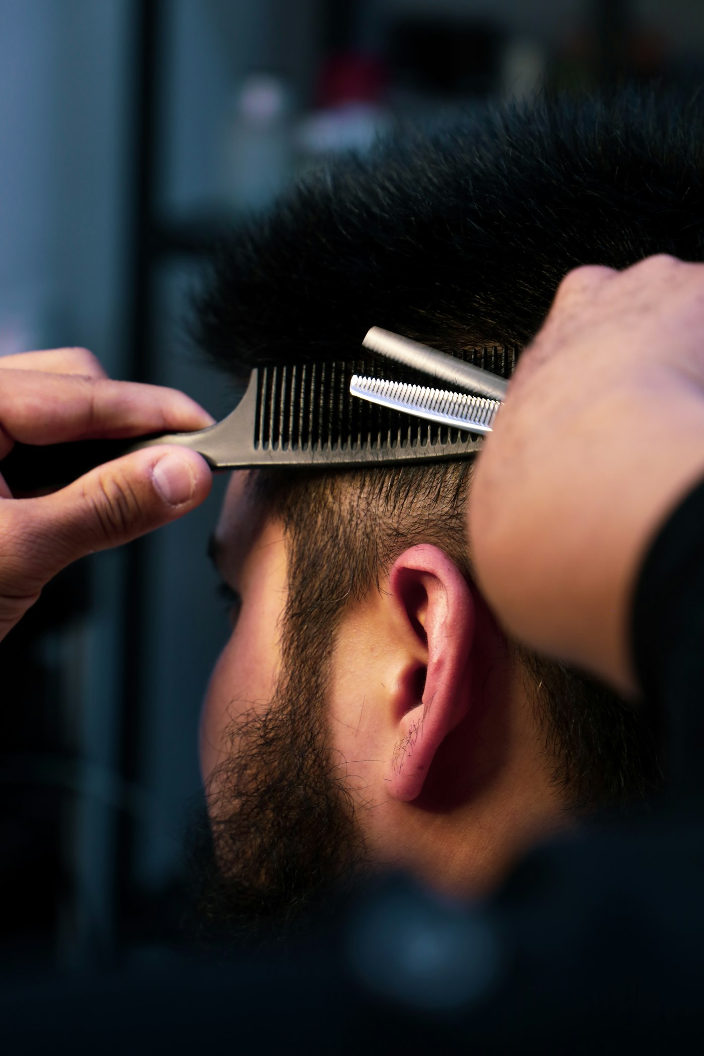 Scissors and a comb cutting the side of a bearded man's hair above the ear