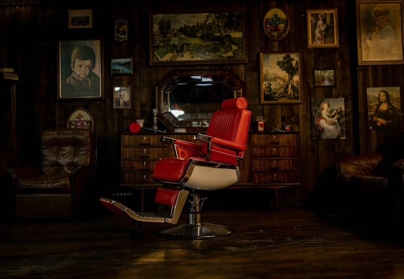 A red vintage barber chair standing empty, with framed pictures on the wall behind it