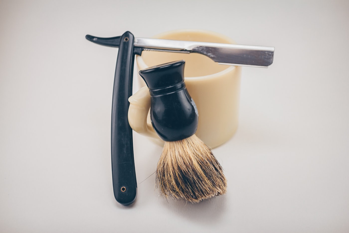 A straight razor and a shaving brush resting against a shaving bowl