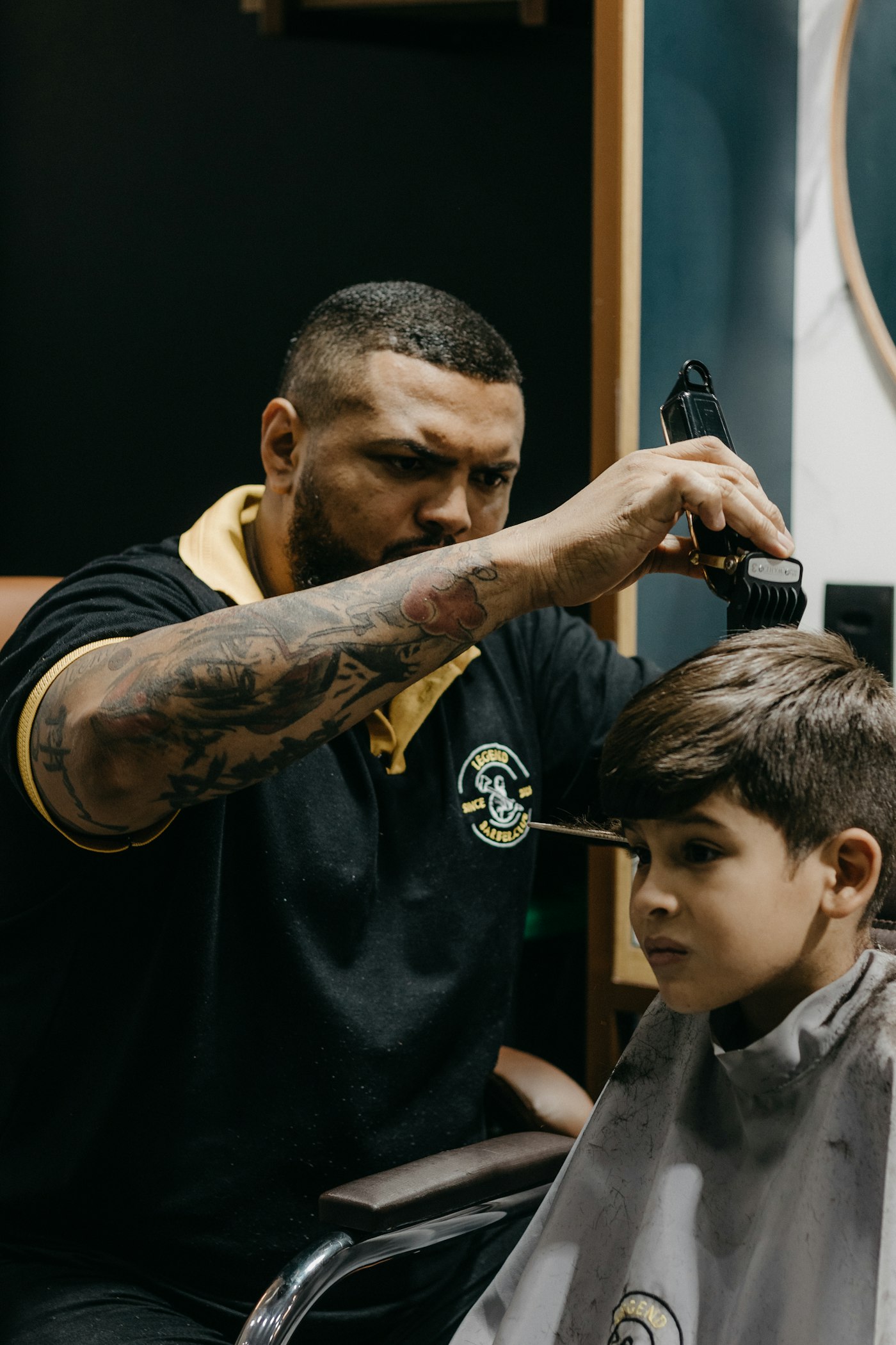 A barber cutting a small boy's hair while the boy sits still in the chair