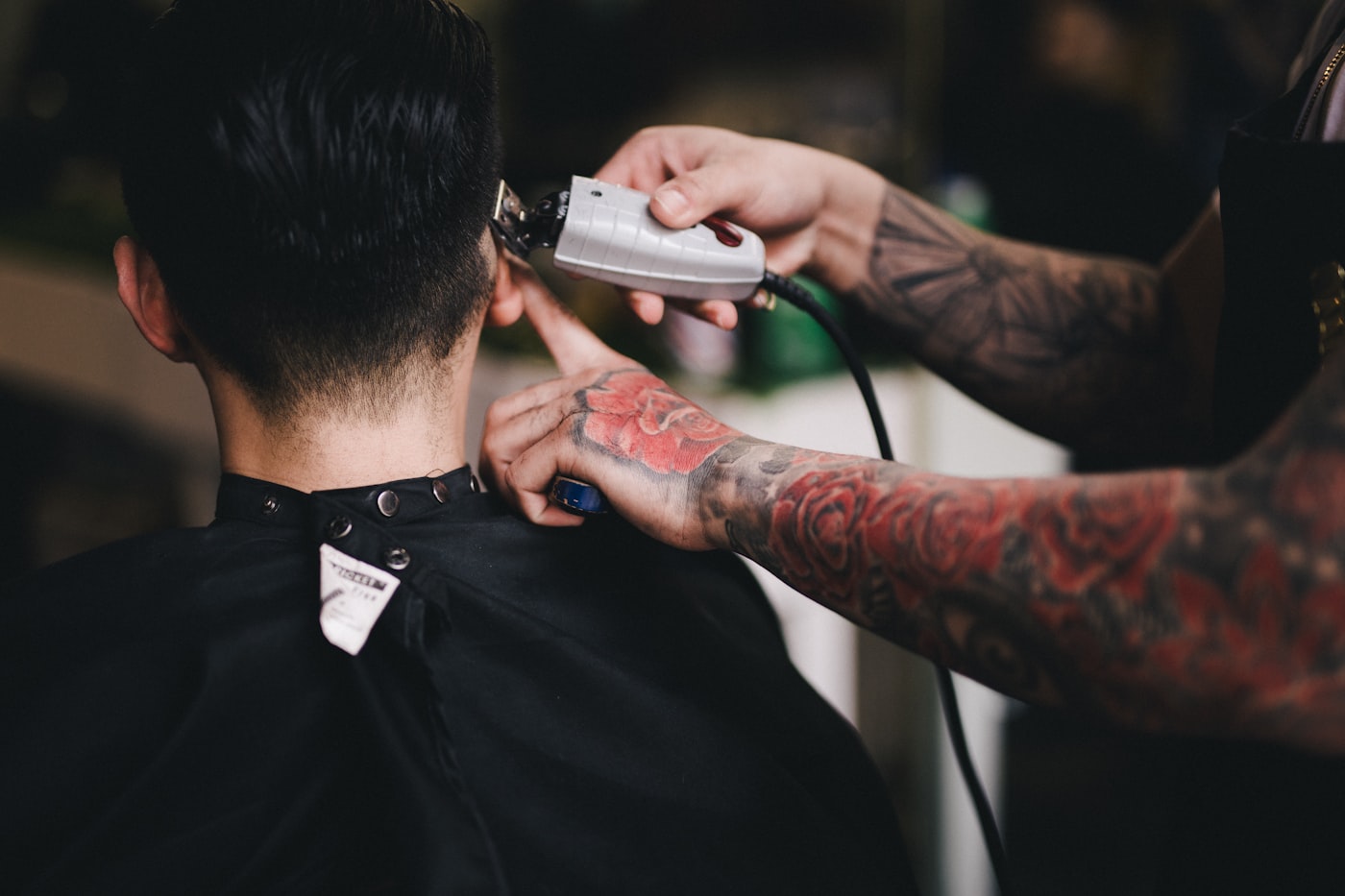 A barber trimming the back of a client's neck with clippers, seen from behind the chair