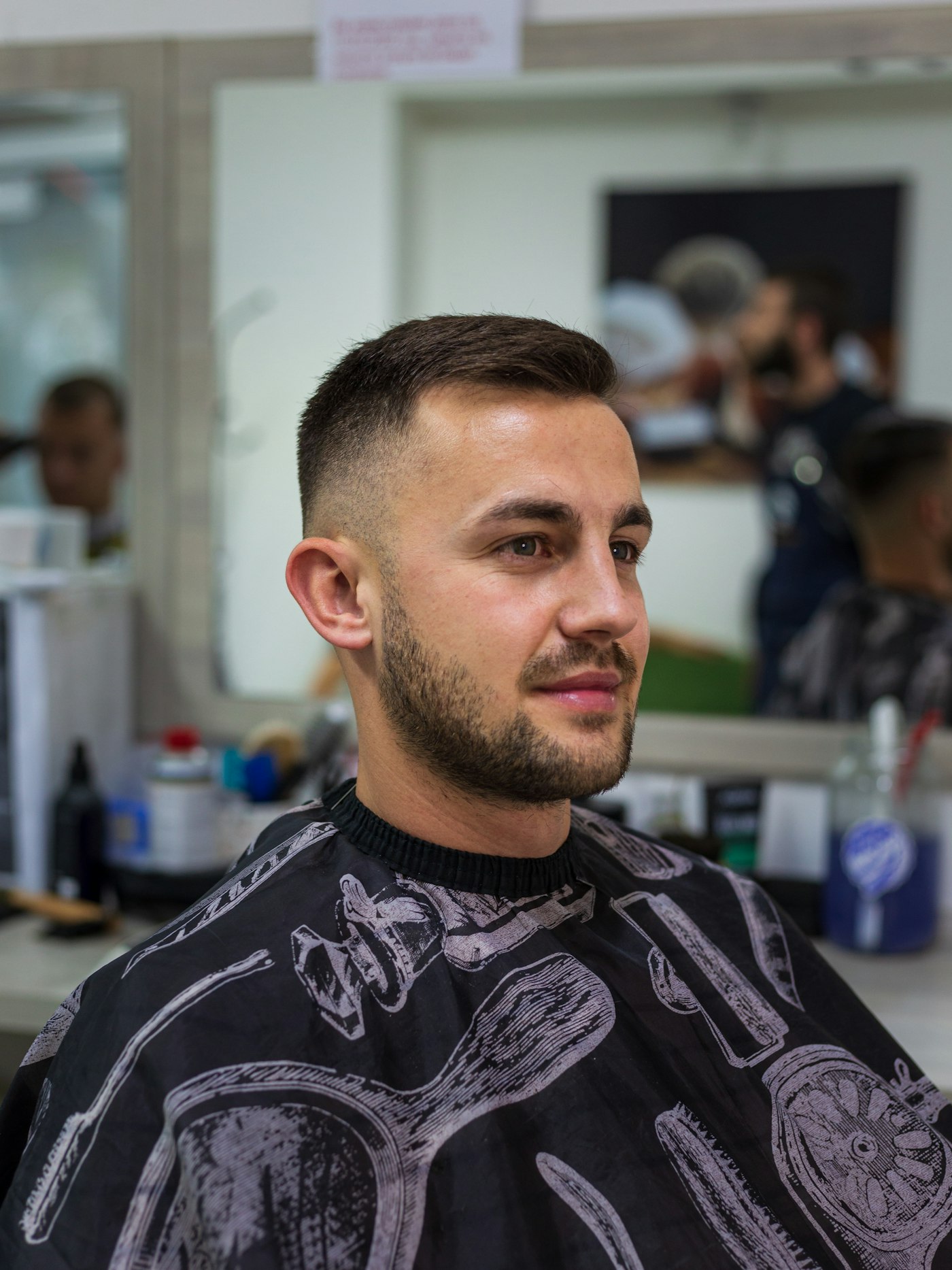 A young man in a barber cape looking at the camera with a finished short haircut