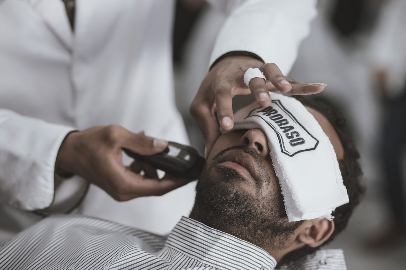 A barber laying a hot towel across a reclined client's face before a shave