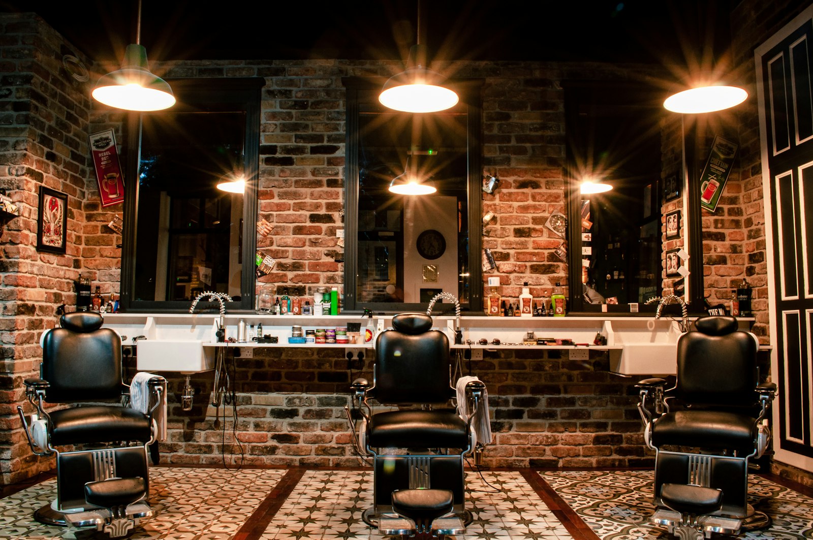 A row of barber chairs and mirrors under round lamps against the shop's brick wall